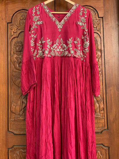 Red dress with silver embroidery on a wooden hanger against a wooden background